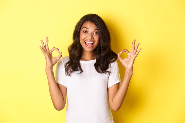 Portrait d'une fille afro-américaine heureuse et heureuse portant un t-shirt blanc montrant des signes corrects