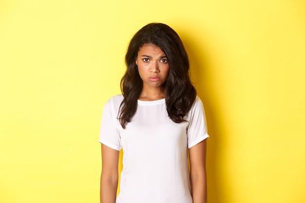 Portrait d'une fille afro-américaine sombre et triste boudant et semblant bouleversée debout en t-shirt blanc