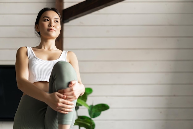 Portrait d'une fille asiatique faisant de l'exercice à la maison en soulevant les jambes et en regardant à distance l'exercice en livi...