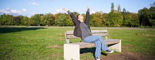 Portrait d'une fille asiatique heureuse ressentant la liberté et l'excitation tendant les mains tout en étant assise sur un banc