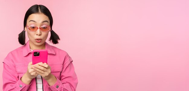 Portrait d'une fille asiatique à lunettes de soleil à l'aide d'un smartphone