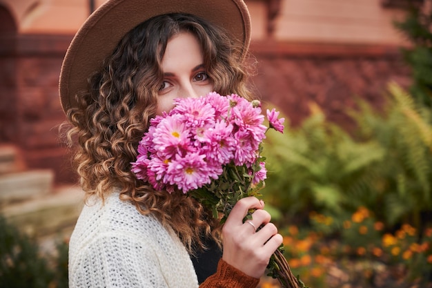 Portrait de fille bouclée avec bouquet de fleurs près du visage