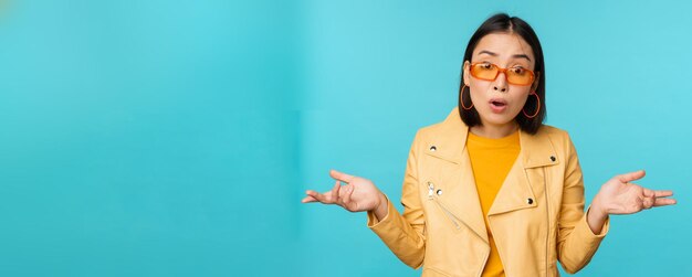 Portrait d'une fille chinoise à lunettes de soleil a l'air confus, hausse les épaules et regarde perplexe la caméra