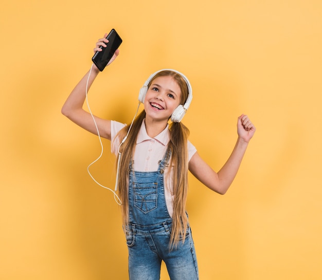 Portrait, fille, danse, tout, écoute, musique, casque, par, téléphone portable, contre, toile de fond jaune