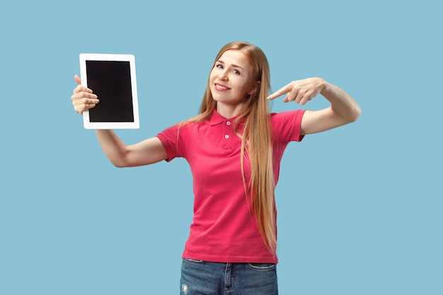 Portrait d'une fille décontractée confiante montrant un écran blanc d'ordinateur portable isolé sur mur bleu