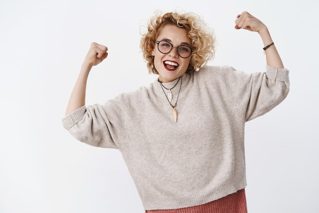 Portrait d'une fille fière qui ressent de la joie de gagner un prix en levant les mains puissantes comme un champion célébrant la victoire et triomphant en souriant largement et en acclamant sans soucis sur un mur blanc.