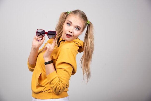 Portrait d'une fille heureuse en sweat à capuche jaune tenant des lunettes.