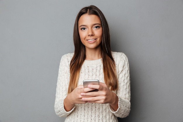 Portrait d'une fille joyeuse en pull tenant un téléphone mobile