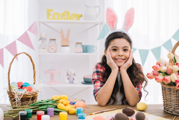 Portrait d&#39;une fille avec des oeufs de Pâques; peinture et fleurs de tulipes sur table