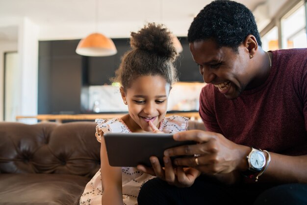 Portrait d'une fille et d'un père s'amusant ensemble et jouant avec une tablette numérique à la maison