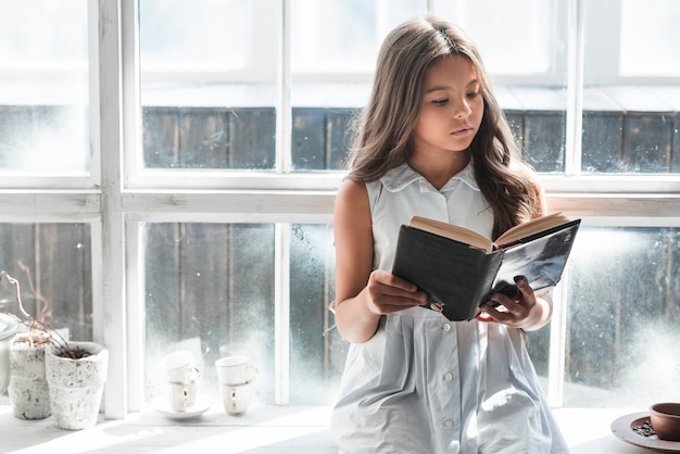 Photo gratuite portrait, fille, séance, fenêtre, lecture, livre