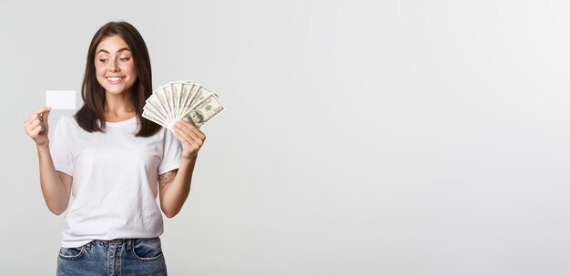 Portrait d'une fille souriante excitée tenant de l'argent et une carte de crédit fond blanc