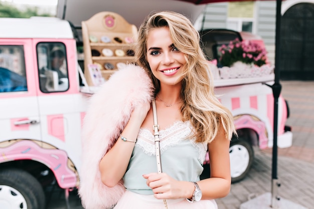 Portrait de fille de style pin up avec de longs cheveux blonds sur fond de voiture de café rétro. Elle sourit à la caméra.