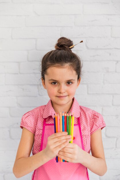 Portrait, fille, tenue, crayons multicolores, main, debout, contre, mur, brique blanche