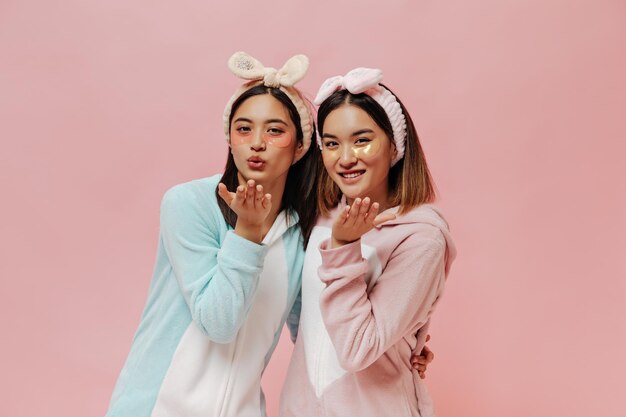 Portrait de filles asiatiques aux cheveux courts dans des bandeaux et avec des cache-œil cosmétiques Jolies femmes en pyjama soufflent un baiser sur fond rose