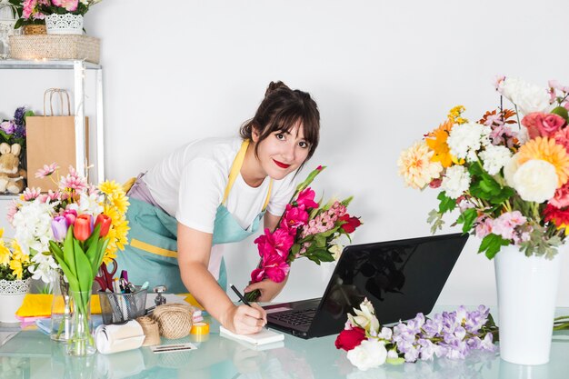 Portrait d&#39;une fleuriste avec des fleurs écrivant sur le bloc-notes