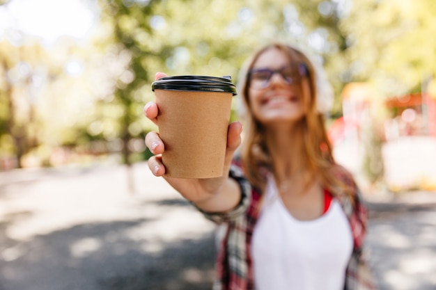 Portrait flou d'adorable femme tenant une tasse de café. Fille élégante insouciante appréciant la journée d'été.