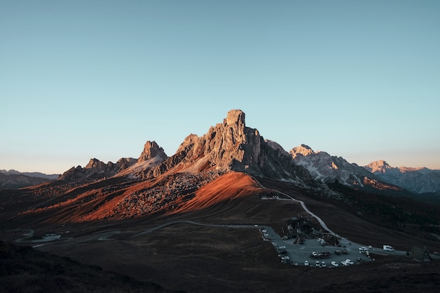 Portrait d'une formation rocheuse brune et de nombreuses voitures garées sous le ciel bleu dans la soirée