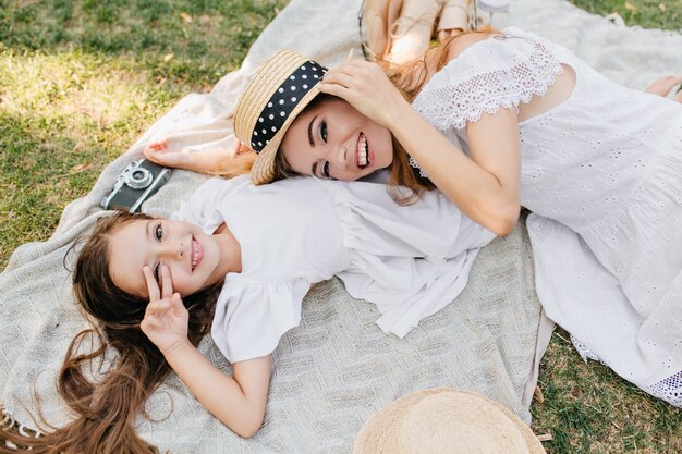 Portrait de frais généraux de filles relaxantes allongé sur une couverture et souriant. Excité jeune femme reposant sur l'herbe jouant avec sa fille joyeuse.