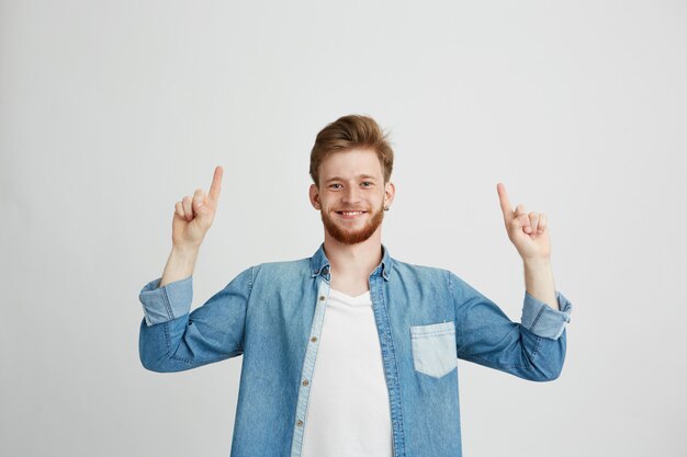 Portrait de gai jeune homme souriant pointant le doigt vers le haut.