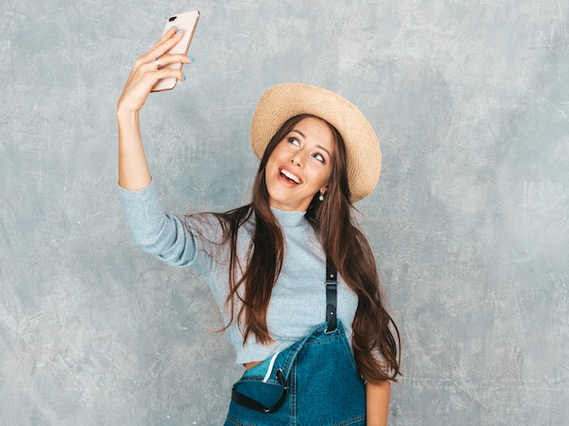 Portrait de gaie jeune femme prenant selfie photo et portant des vêtements modernes et un chapeau.