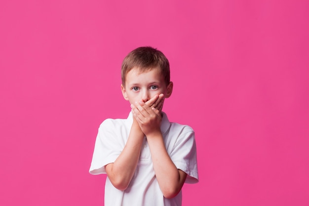 Photo gratuite portrait de garçon couvrant sa bouche sur fond rose