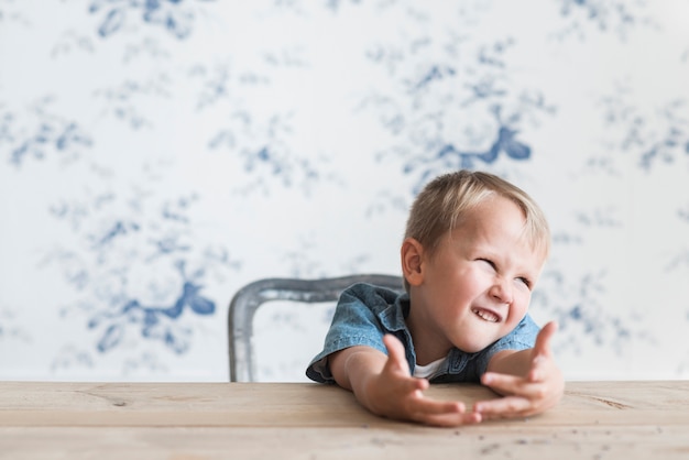 Photo gratuite portrait d'un garçon faisant la grimace, assis devant un papier peint