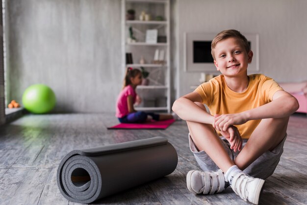 Portrait d&#39;un garçon souriant assis près du tapis d&#39;exercice enroulé