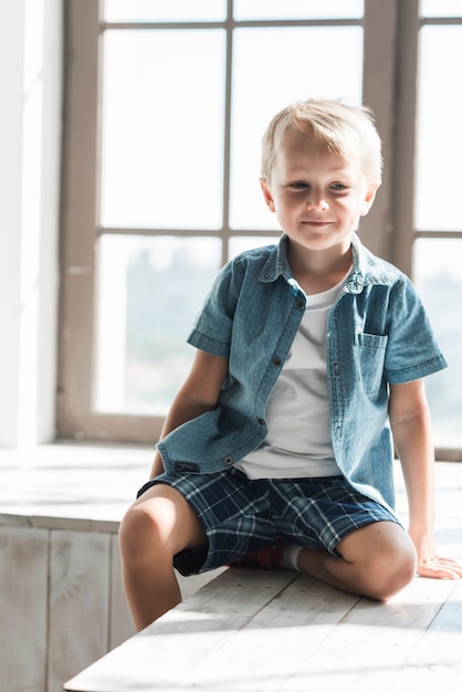 Photo gratuite portrait d'un garçon souriant assis près de la fenêtre