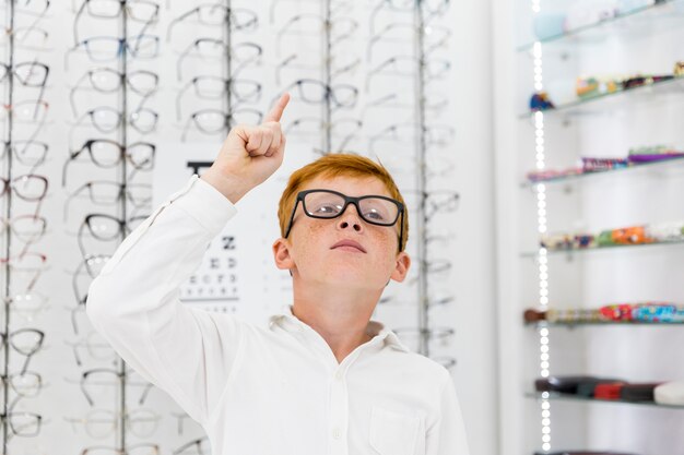 Portrait de garçon de taches de rousseur pointant vers le haut dans le magasin d'optique