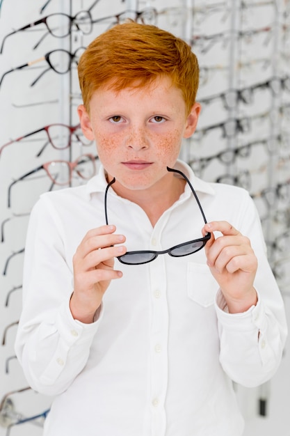 Portrait de garçon de taches de rousseur en regardant la caméra tout en tenant des lunettes