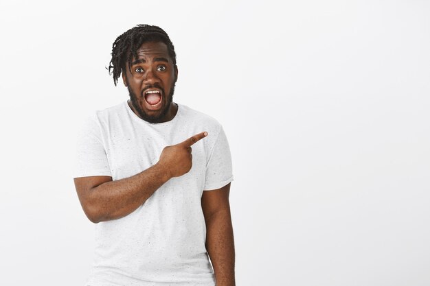 Portrait de gars choqué avec des tresses posant contre le mur blanc