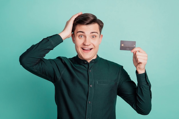 Portrait de gars drôle excité tenir la tête de la carte de débit réaction folle sur fond bleu sarcelle