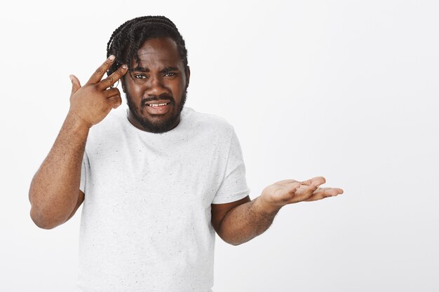 Portrait de gars frustré avec des tresses posant contre le mur blanc