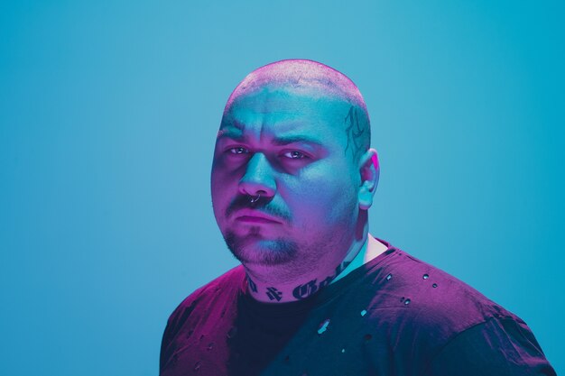 Portrait d'un gars hipster avec néon coloré sur mur bleu. Modèle masculin d'humeur calme et sérieuse.