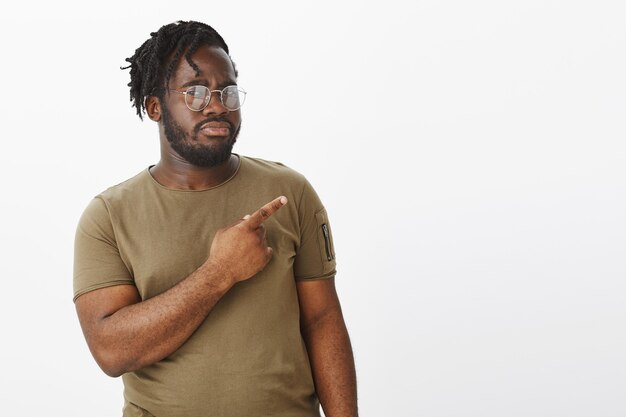 Portrait de gars incertain avec des lunettes posant contre le mur blanc