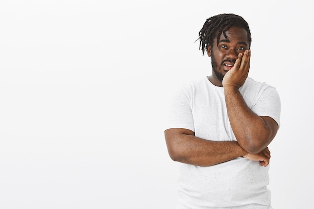 Portrait de gars non impressionné avec des tresses posant contre le mur blanc