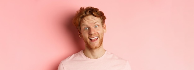 Portrait d'un gars rousse drôle montrant la langue faisant des grimaces idiotes à l'appareil photo debout joyeux contre pi