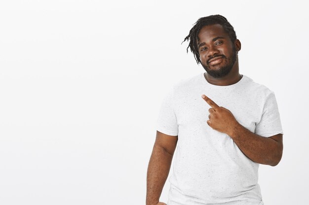 Portrait de gars satisfait avec des tresses posant contre le mur blanc