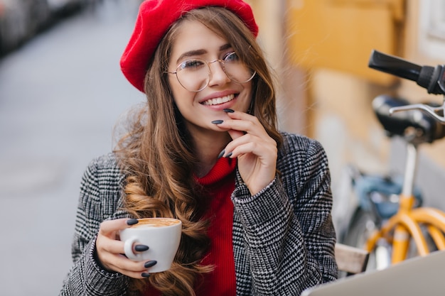 Portrait en gros plan de l'adorable jeune femme avec manucure noire posant avec une tasse de café chaud