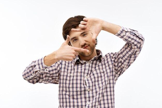 Portrait en gros plan d'un beau jeune homme aux cheveux noirs aux yeux bleus et confiant portant une chemise à carreaux décontractée regardant l'avant faisant le cadre avec ses mains