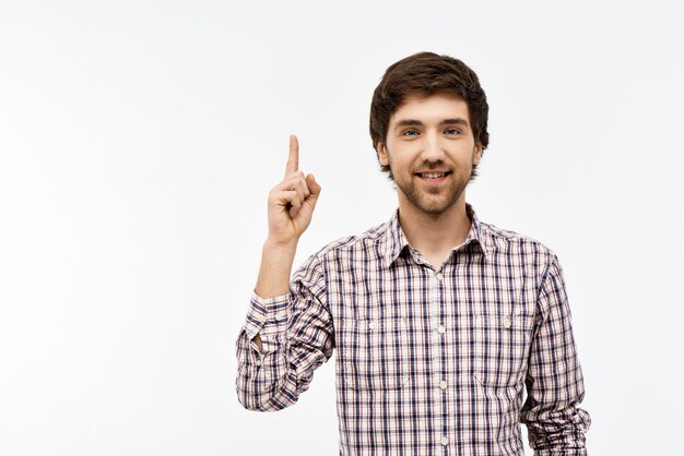 Portrait en gros plan d'un beau jeune homme aux cheveux noirs aux yeux bleus et confiant portant une chemise à carreaux décontractée regardant vers l'avant, pointant vers le haut