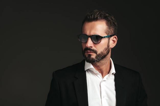 Portrait en gros plan d'un beau modèle lambersexuel hipster élégant et confiant Sexy homme moderne vêtu d'un élégant costume noir Mode masculine posant en studio sur fond sombre