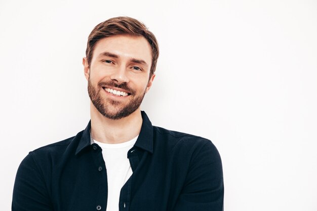 Portrait en gros plan d'un beau modèle souriant Sexy homme élégant vêtu d'une chemise et d'un jean Mode hipster mâle posant près d'un mur blanc en studio Isolé