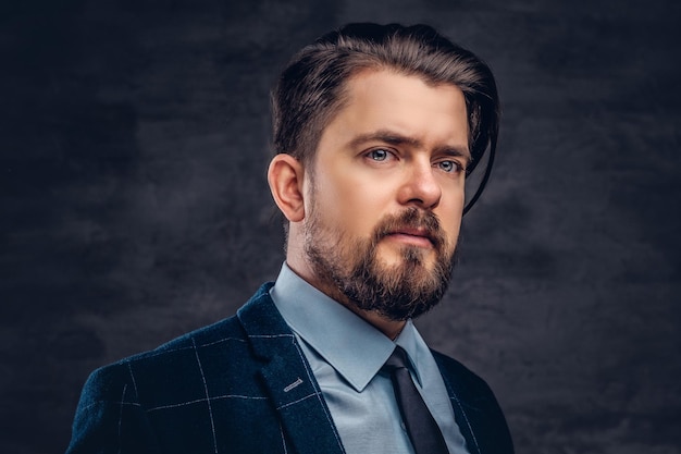 Portrait en gros plan d'un bel homme d'âge moyen avec barbe et coiffure vêtu d'un élégant costume formel sur un fond sombre texturé en studio.