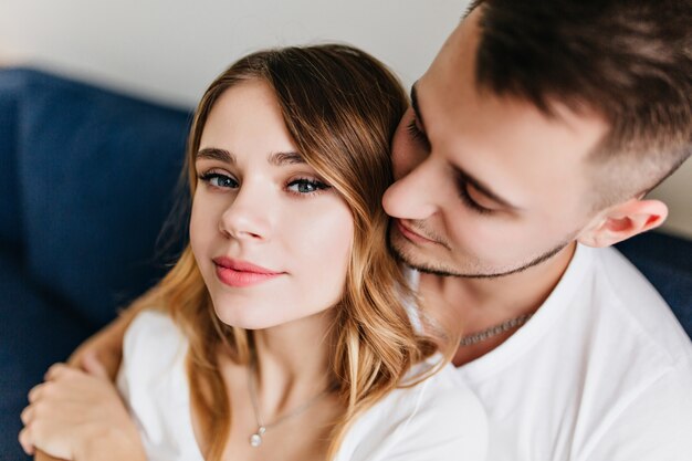 Portrait de gros plan de bel homme européen embrassant une fille séduisante. Plan intérieur d'une femme blonde détendue passant du temps libre avec son petit ami.