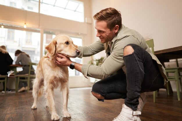 Portrait en gros plan d'un bel homme heureux caressant son mignon chien dans un café adapté aux animaux