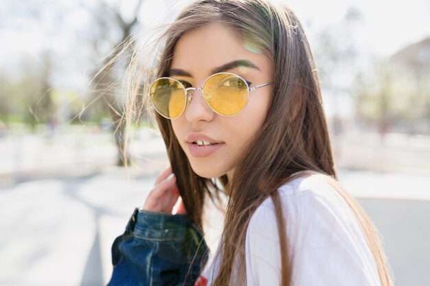 Portrait en gros plan de la belle femme aux longs cheveux brun clair et aux grands yeux porte des spectateurs élégants jaunes