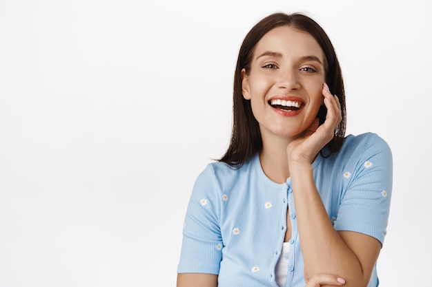 Portrait en gros plan d'une belle femme brune en riant, touchant une peau du visage saine et éclatante parfaite et des dents blanches souriantes, ravie d'un traitement anti-âge dans un salon de spa, soldes d'été.