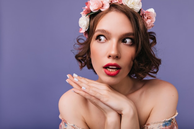 Portrait de gros plan de belle femme rêveuse avec des roses dans les cheveux. Photo intérieure d'une fille merveilleuse en couronne debout.